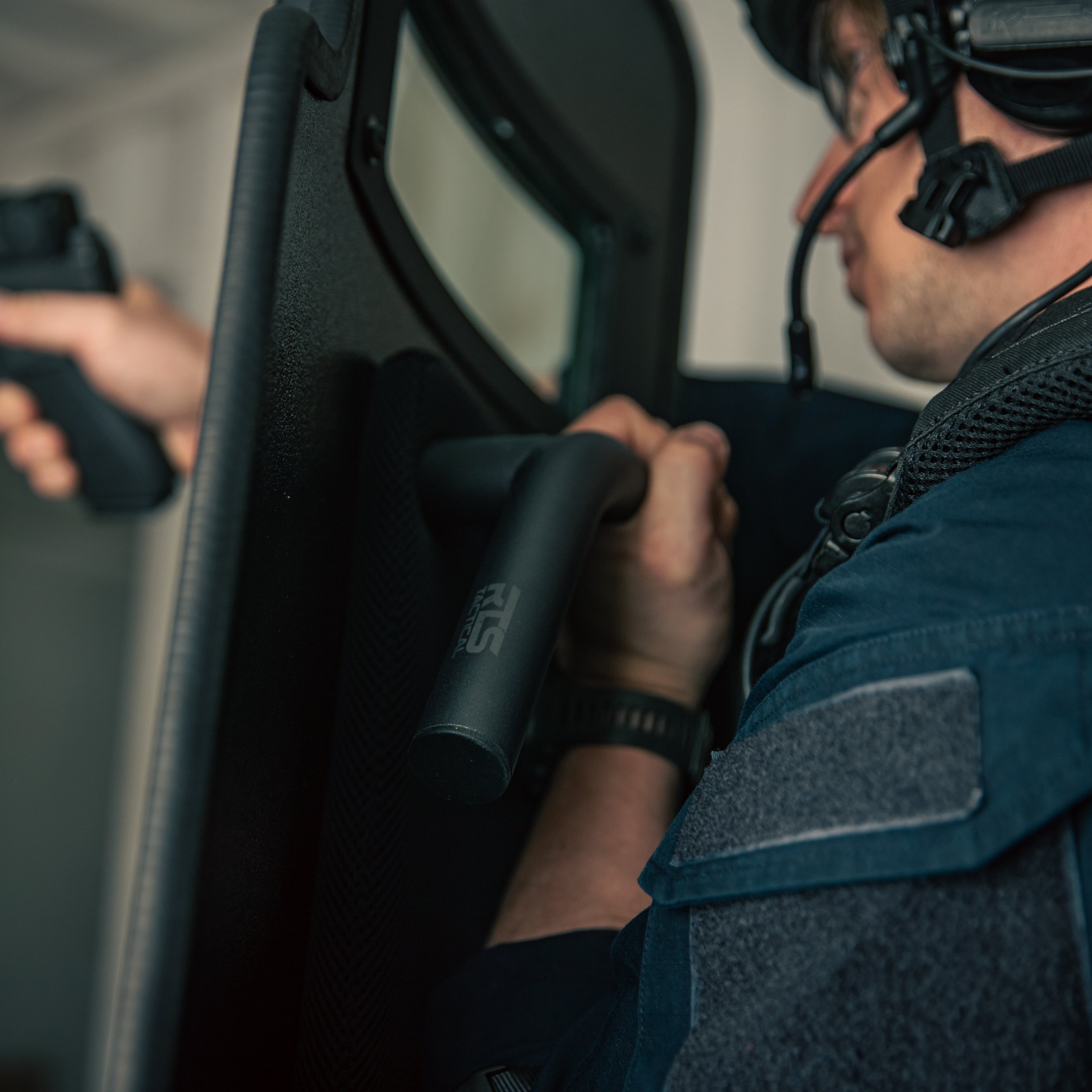 A tactical officer holding a handgun while bracing behind a ballistic shield
