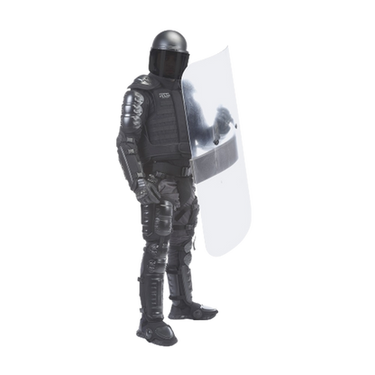 A person in full black riot gear stands holding a large clear shield. The gear includes a helmet and padded armor.