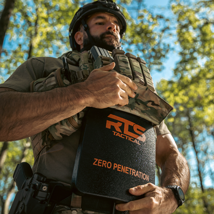 Man in tactical gear adjusts a vest, holding armor plate.