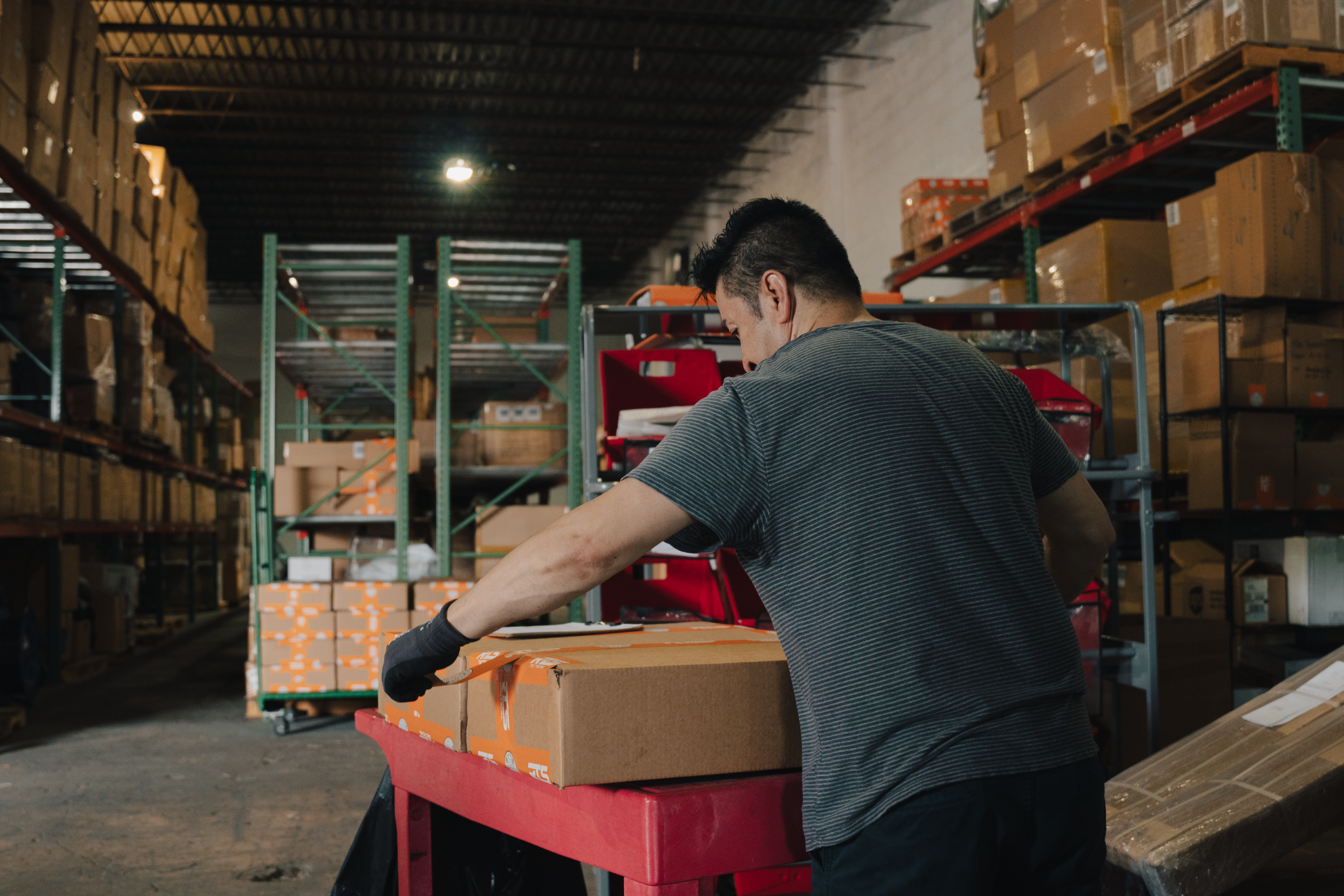 A worker packing boxes in a warehouse, surrounded by shelves stacked with packages.