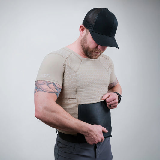 A muscular man wearing a beige fitted top and a body armor compression shirt underneath
