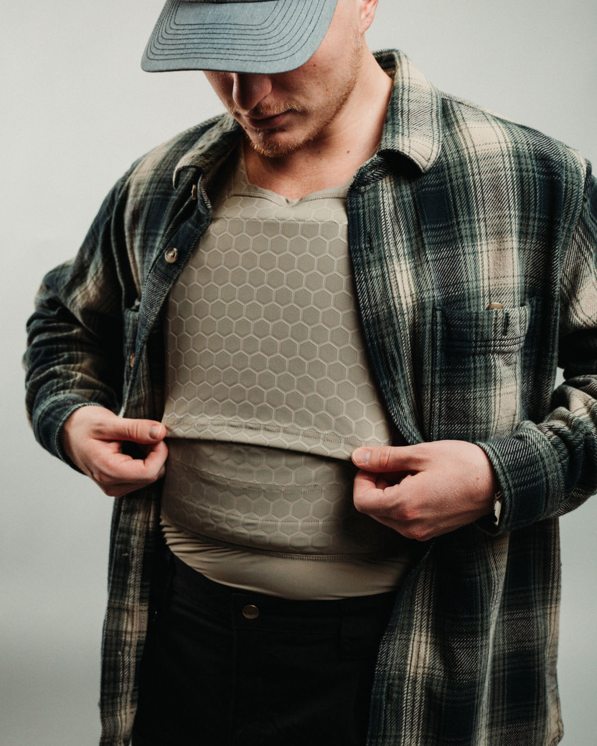 Person wearing a denim cap and plaid shirt adjusting a compression shirt for protection.