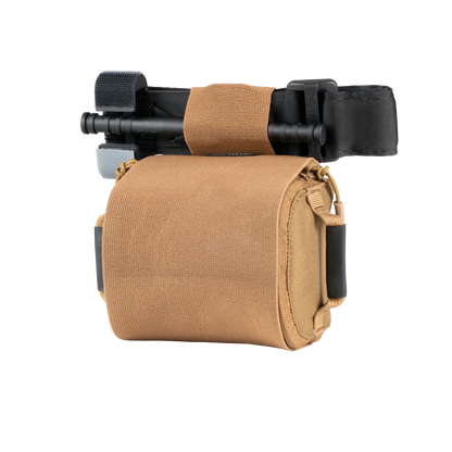 Tan tactical pouch with a black tourniquet secured on top. The pouch is compact, sturdy, and designed for emergency medical use.