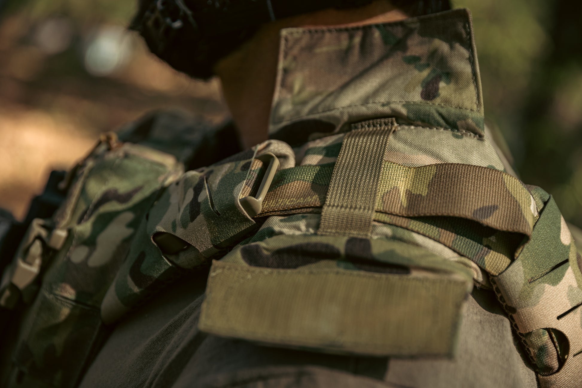 Close-up of a person wearing a camouflage tactical vest in a forest setting. The vest features straps and pouches, conveying readiness and alertness.