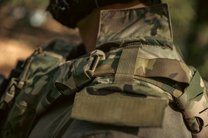Close-up of a person wearing a camouflage tactical vest in a forest setting. The vest features straps and pouches, conveying readiness and alertness.