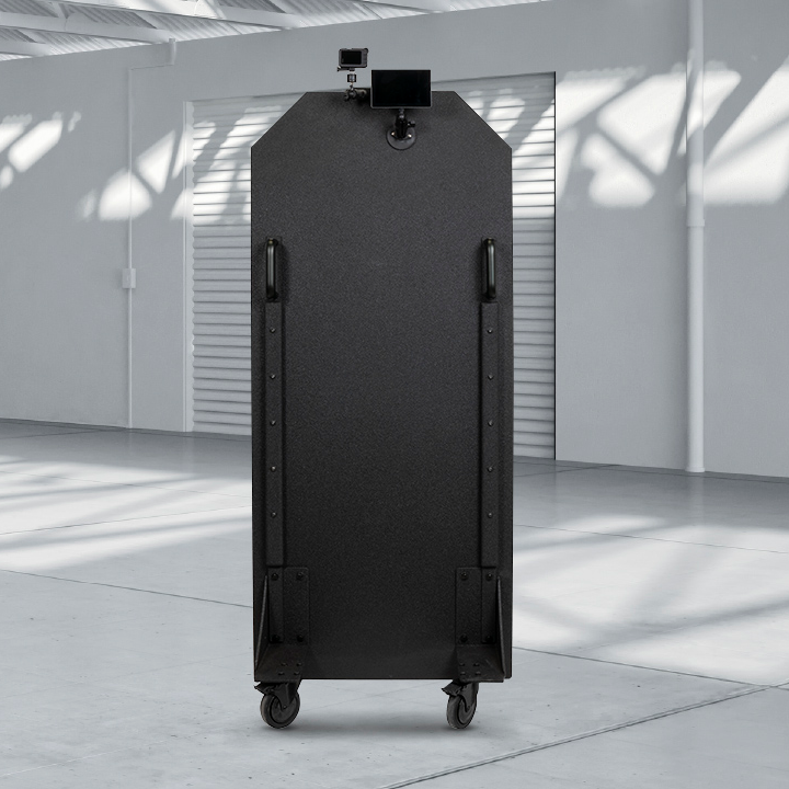 A tall, black, bulletproof panel is positioned in a spacious, sun-lit industrial warehouse.