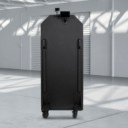 A tall, black, bulletproof panel is positioned in a spacious, sun-lit industrial warehouse.