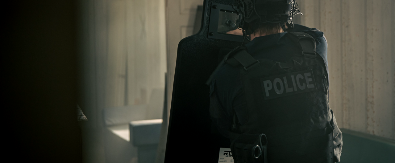 A man wearing a black premium plate carrier holding an RTS Tactical ballistic shield.