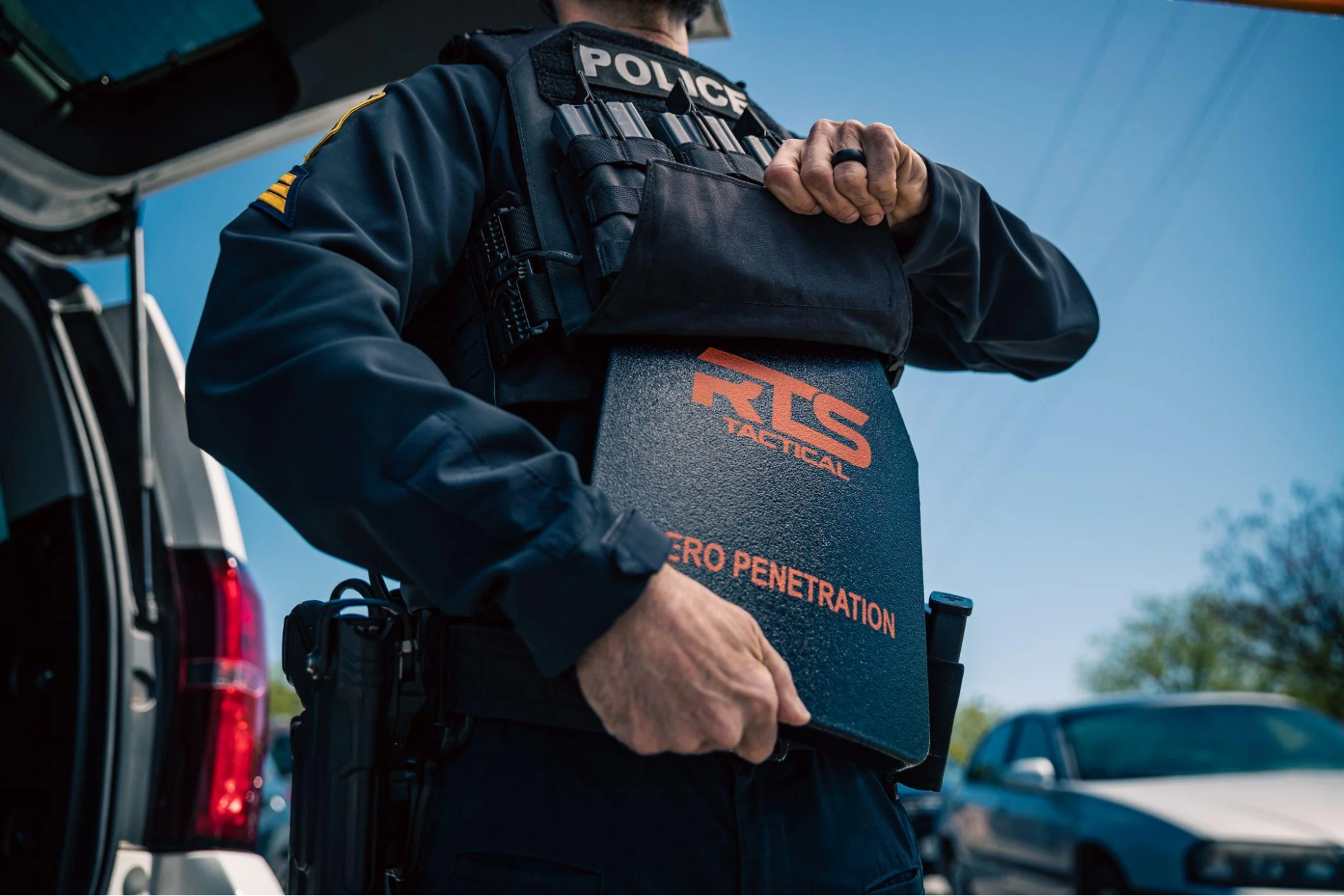 A police officer is pulling a tactical shield from a vest while standing next to a car.