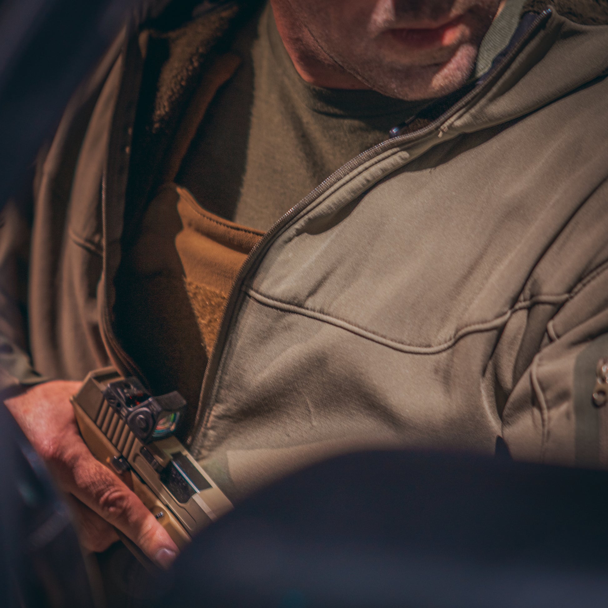 A person in a jacket conceals a handgun in an inner pocket. The scene conveys tension and readiness, with muted tones and focused lighting.