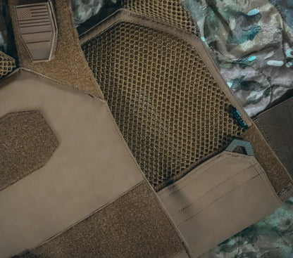 Close-up of tactical gear featuring a brown textured vest with mesh panels and Velcro patches, set against a camouflage fabric background.