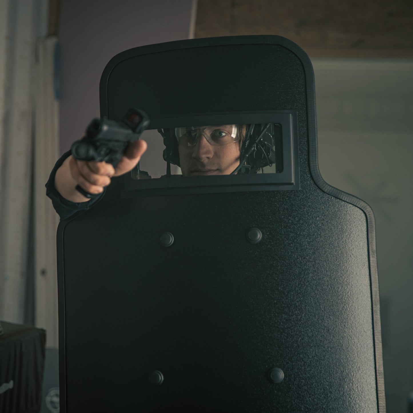 Policeman behind a ballistic shield aiming a firearm