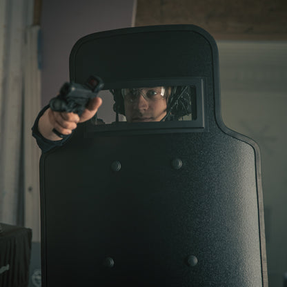 Policeman behind a ballistic shield aiming a firearm