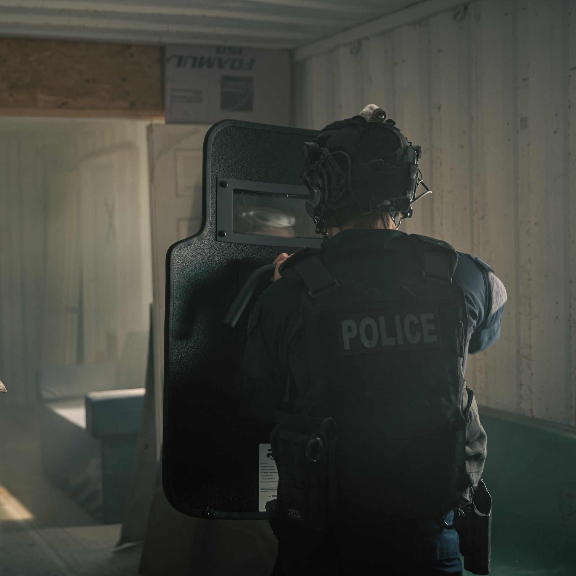 A police officer in tactical gear holding a shield, preparing to enter an area