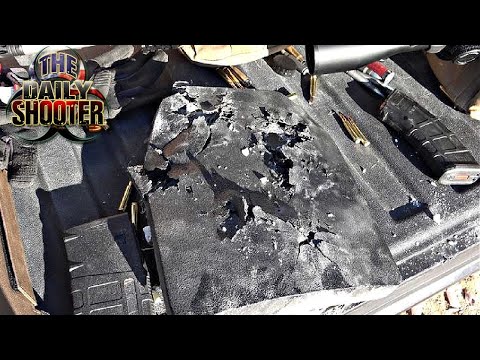 A damaged bulletproof plate with visible holes and cracks lies on a vehicle seat, surrounded by scattered bullet cartridges.